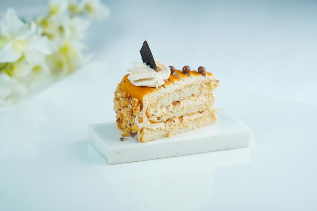 Delicious slice of cake with caramel topping, nuts, and chocolate accent on a white plate.