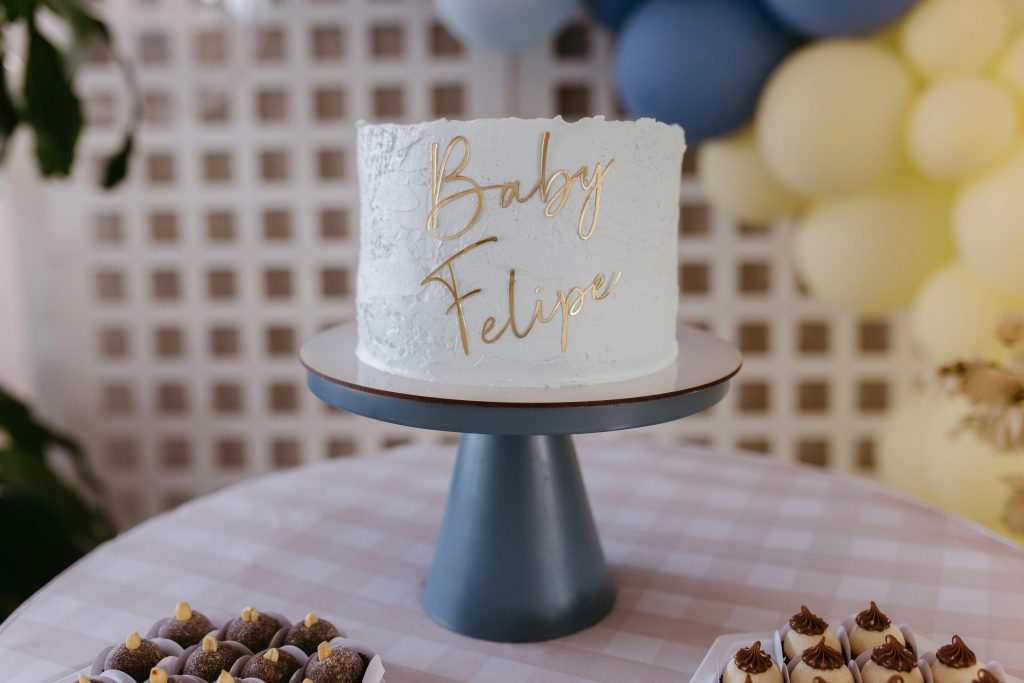 White cake with Baby Felipe inscription surrounded by pastel balloons at a baby shower.