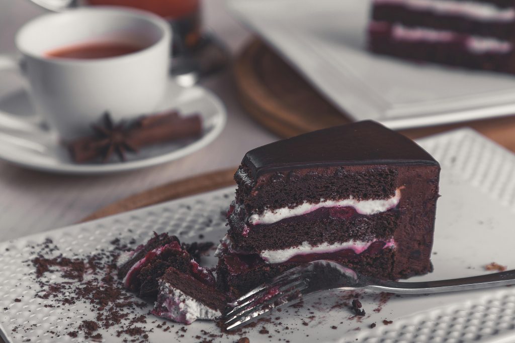 Closeup of a rich chocolate cake slice on a plate with a tea cup in the background.